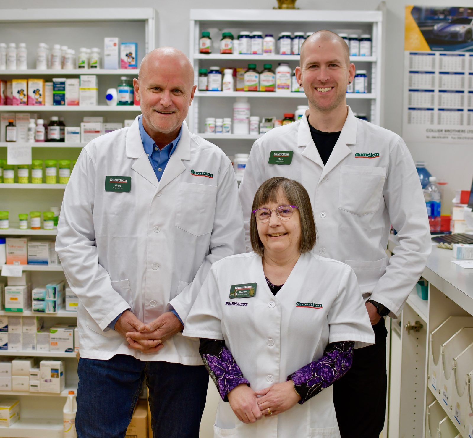 Three Ryan's Pharmacy pharmacists in white coats in front of the medicine wall